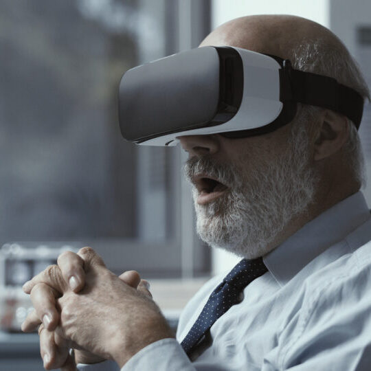 Excited mature businessman wearing a VR headset and experiencing virtual reality in his office