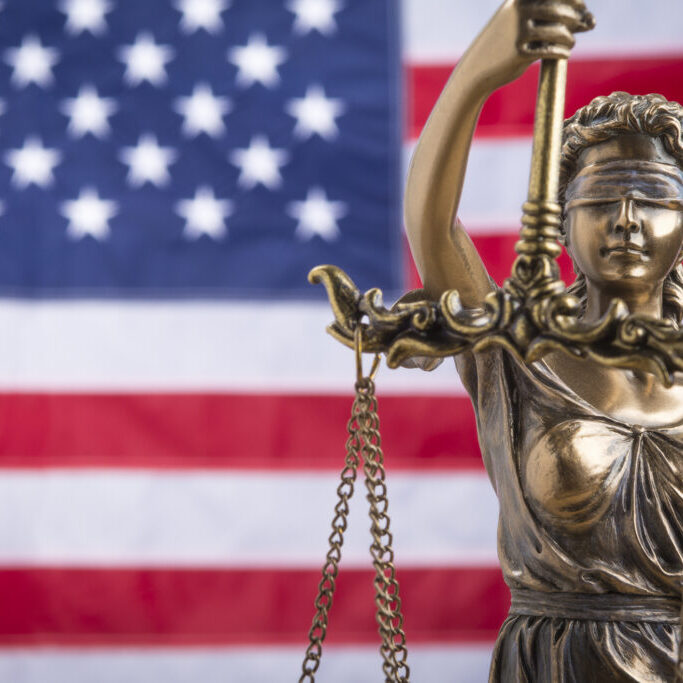 The statue of justice Themis or Justitia, the blindfolded goddess of justice against a flag of the United States of America, as a legal concept