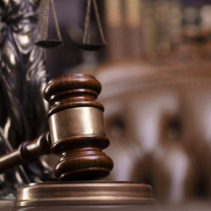 Judge’s gavel, Themis sculpture and collection of legal books on the brown background.